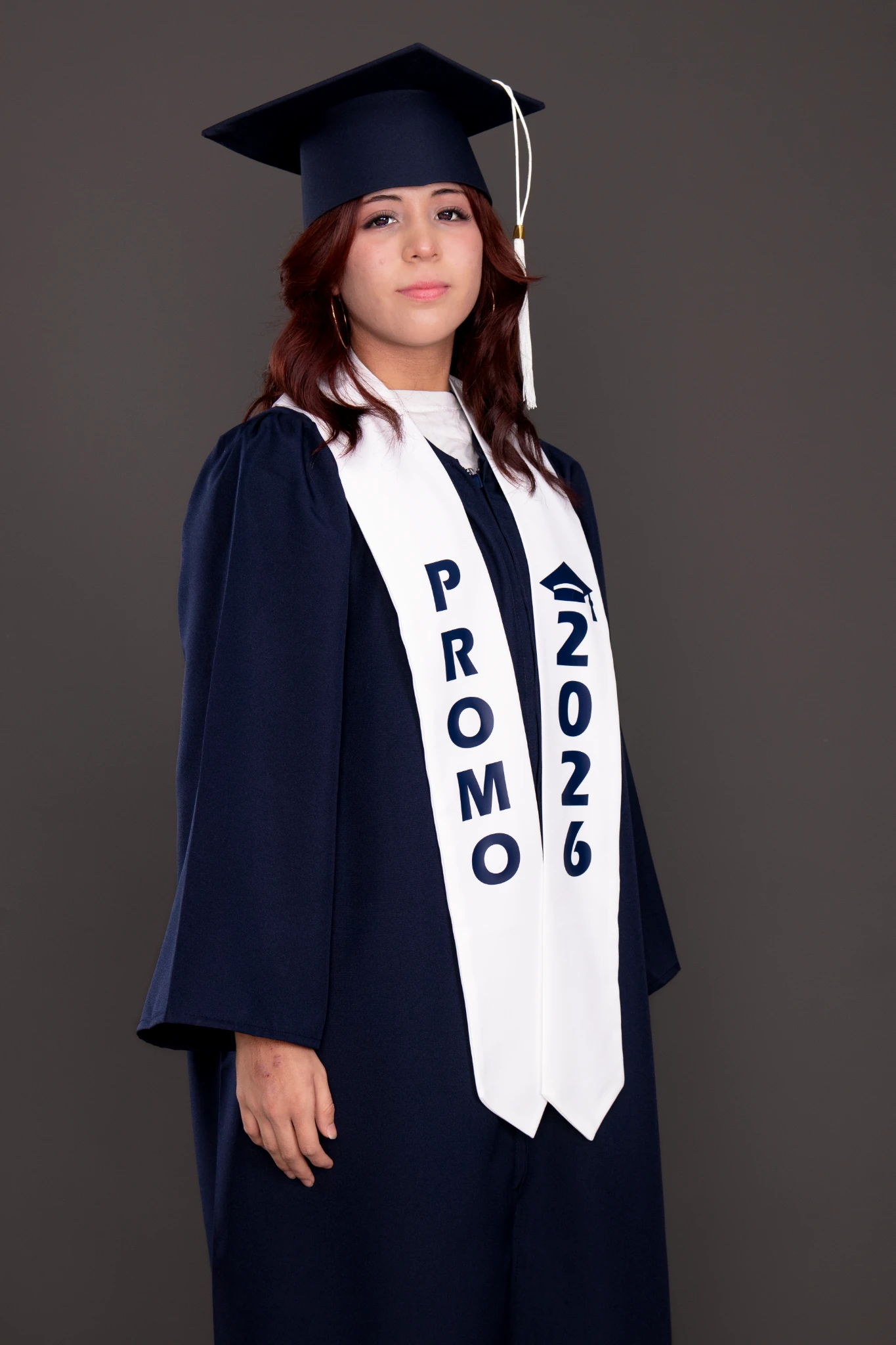 Alumna de promoción escolar 2026 con toga azul, birrete y estola blanca