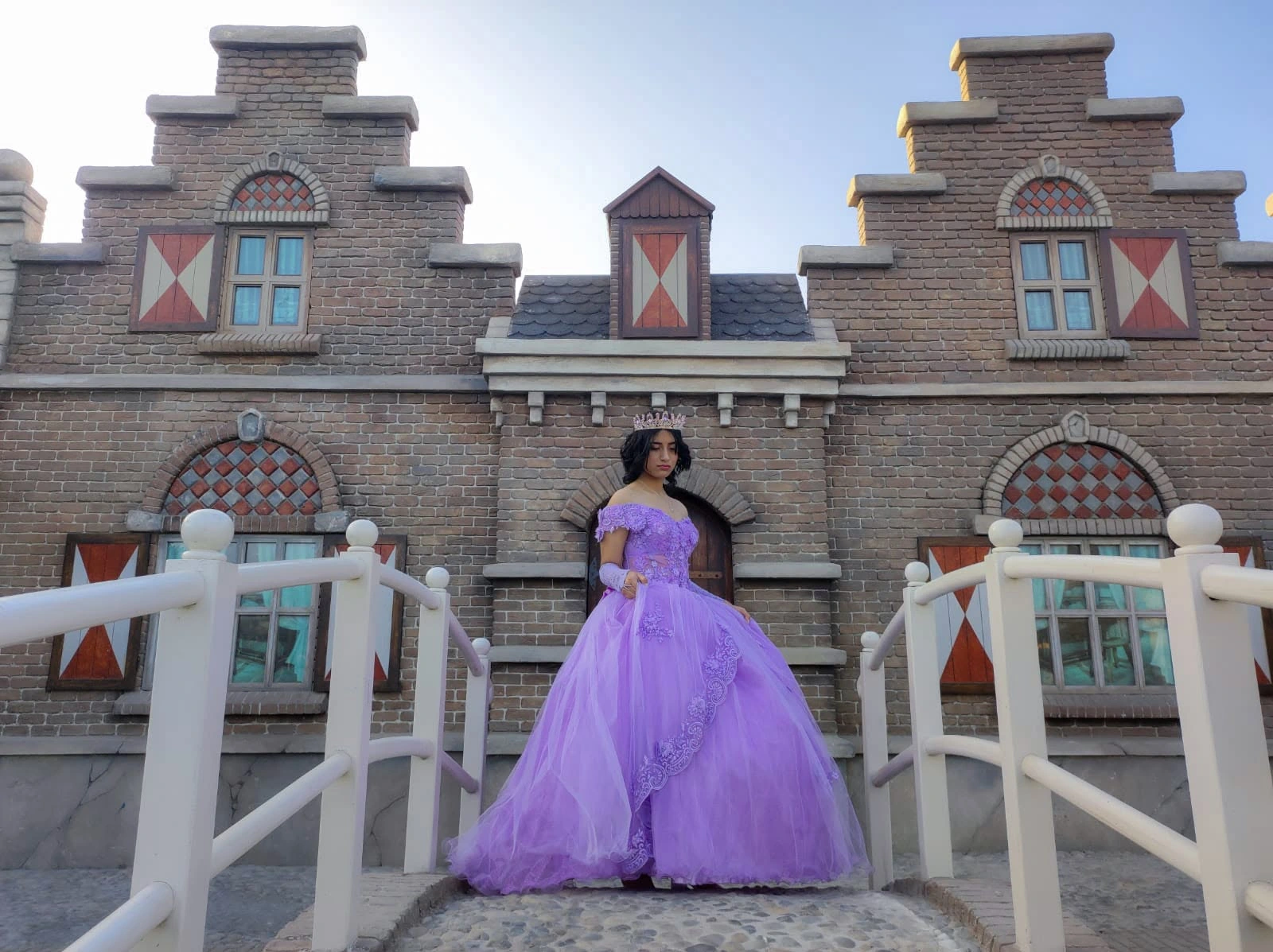 Quinceañera de vestido lila frente a un castillo